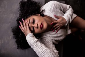 Boudoir image of woman laying back with eyes closed. She is wearing a white sweater and has red nails and lipstick